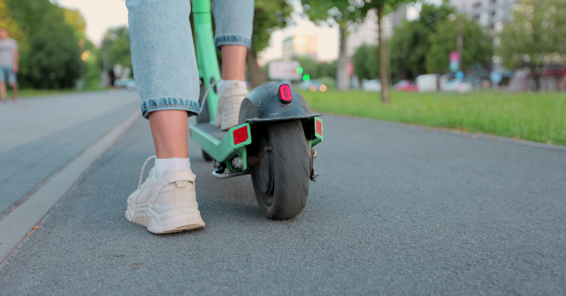 Two legs, one on ground and the other on e-scooter