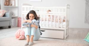 Mother on floor in front of cot with arms wrapped around legs